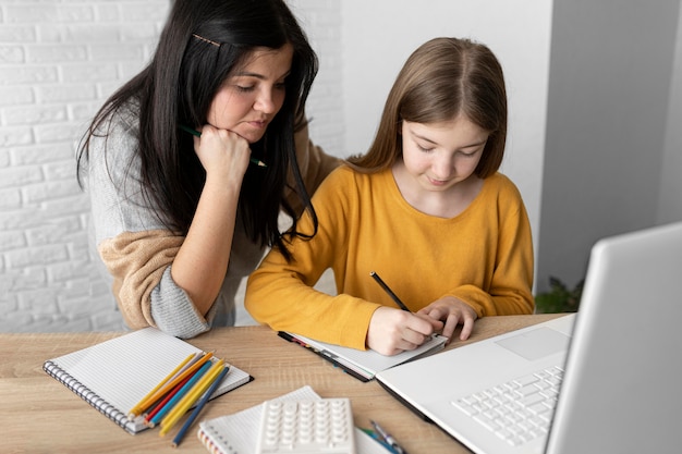 Medium shot woman looking at girl writing