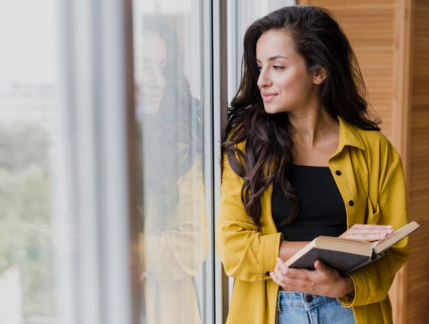 Donna del colpo medio vicino alla finestra con il libro