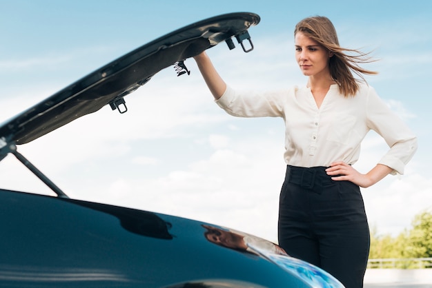 Medium shot of woman opening car hood