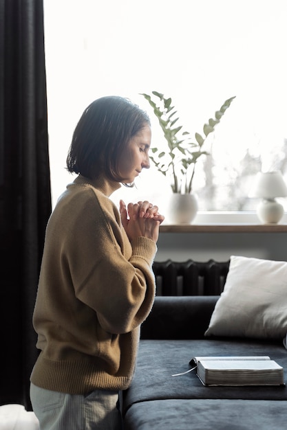 居間で祈るミディアムショットの女性