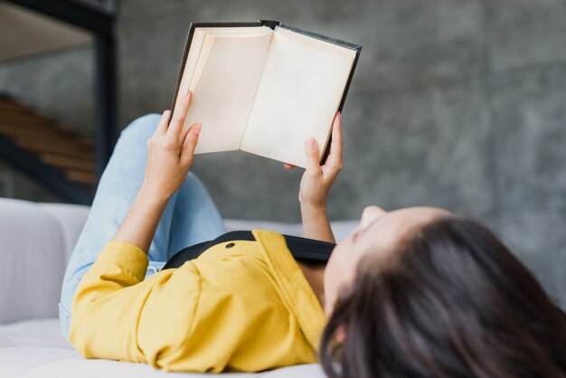 Medium shot woman reading on the couch