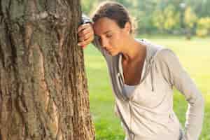 Foto gratuita donna del colpo medio che riposa vicino ad un albero