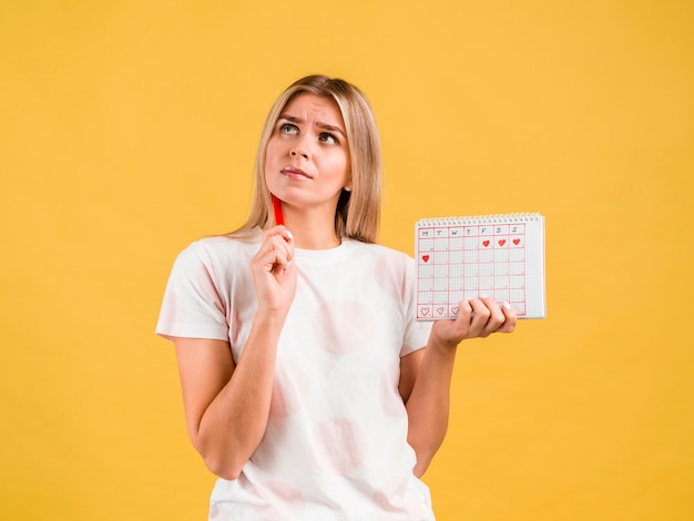 Medium shot of woman thinking and holding  the period calendar
