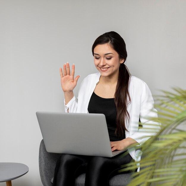 ノートパソコンで手を振っているミディアムショットの女性