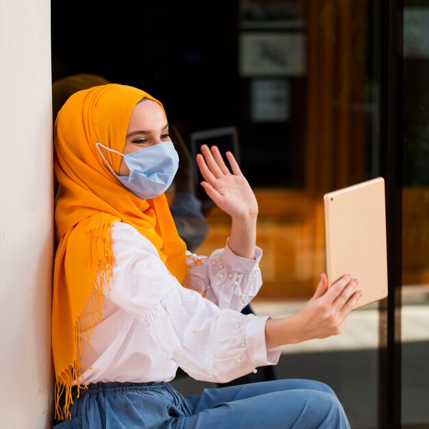 Medium shot woman waving at tablet