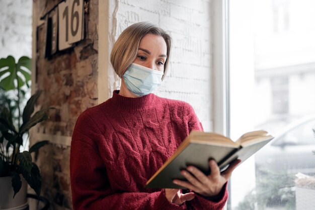 屋内で読書をしているマスクを持つミディアムショットの女性