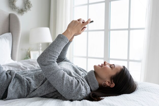 Женщина среднего роста со смартфоном в постели