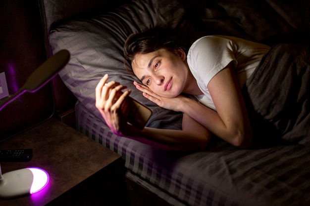 Medium shot woman with smartphone in the bedroom