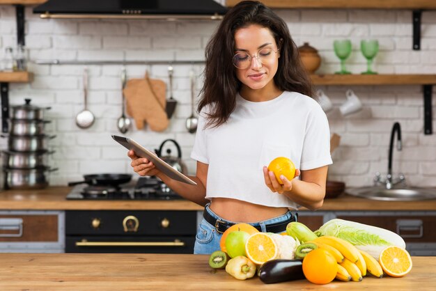 Medium shot woman with tablet looking at an orange