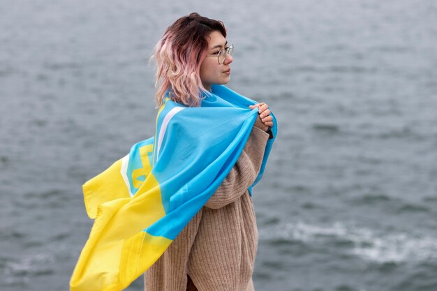 Medium shot woman with ukrainian flag at seaside