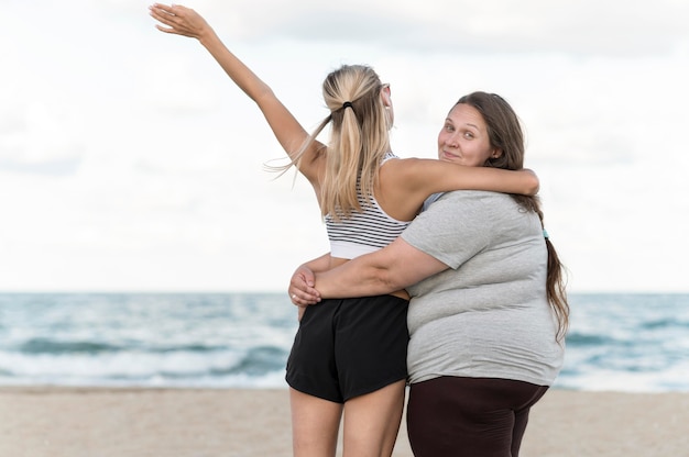 Donne del colpo medio che abbracciano alla spiaggia