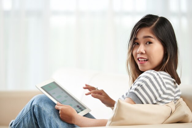Medium shot of young Asian girl turning to look at camera distracted from her tablet PC