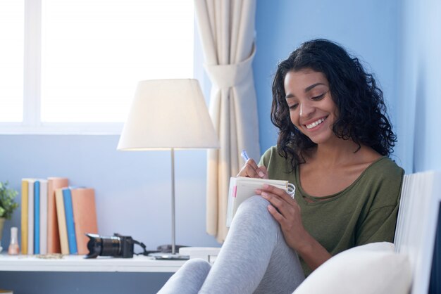 Medium shot of young girl making notes casually resting on couch in her room