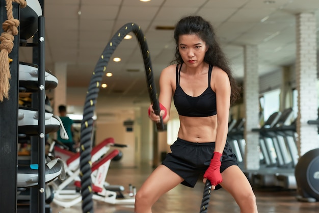 Medium shot of young sportswoman doing crossfit rope exercise