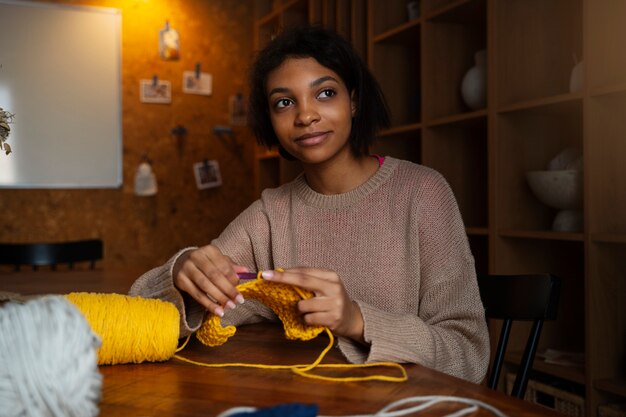 Medium shot young woman crocheting at home