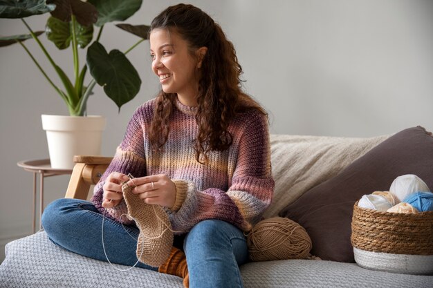 Medium shot young woman knitting on couch