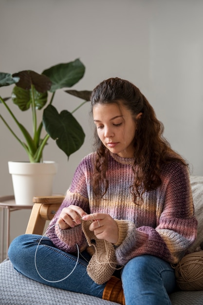 Medium shot young woman knitting at home