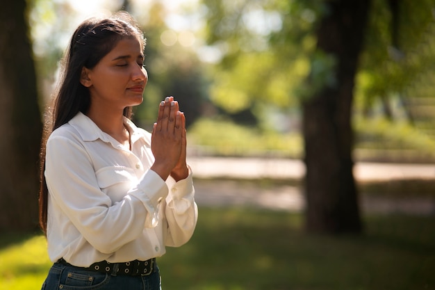 Medium shot young woman praying outdoors