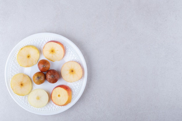 Мушмула и нарезанные яблоки на тарелке, на мраморе.