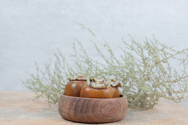 Medlar fruit in bowl with grass on marble table.