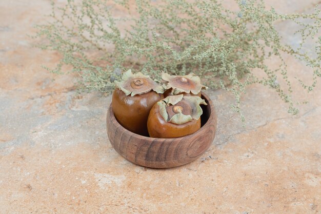 Medlar fruit in bowl with grass on orange surface.