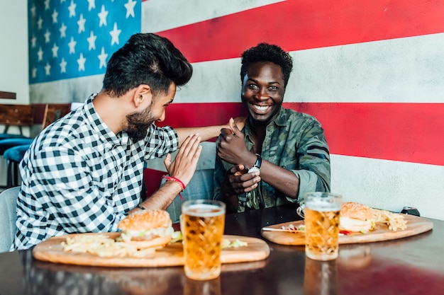 Meet after work.Two smiling boys having fun while spending time with friends in a pub and drinking beer.