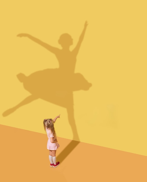 Meeting the future. Childhood and dream concept. Conceptual image with child and shadow on the yellow studio wall. Little girl want to become ballerina, ballet dancer, artist and to build a career.