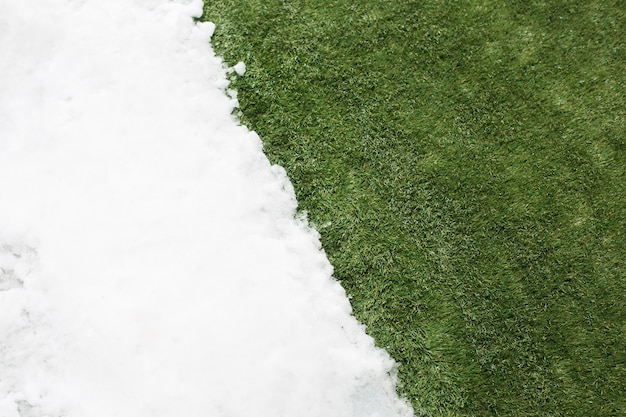 白い雪と緑の草に出会うクローズアップ。冬と春のコンセプトの背景の間。