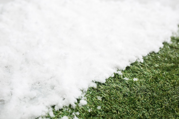 白い雪と緑の草に出会うクローズアップ。冬と春のコンセプトの背景の間。