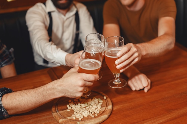 親友との出会い。カジュアルな服装で3人の幸せな若い男性が一緒にバーに座って話したり、ビールを飲んだりします。
