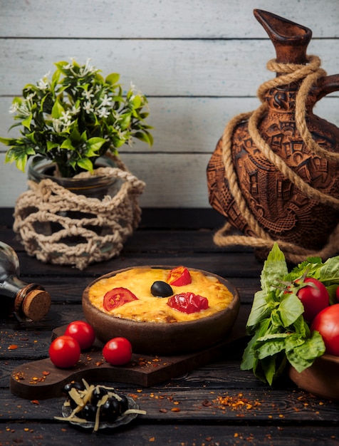 Free photo melted cheese topped with tomato slices and olive in pottery pan