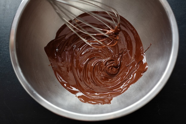 Melted chocolate in pot with chocolate pieces around. Closeup.