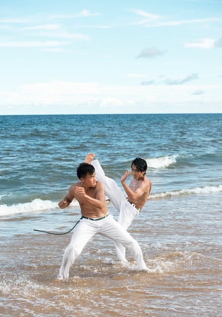 Free photo men by the beach practicing capoeira together