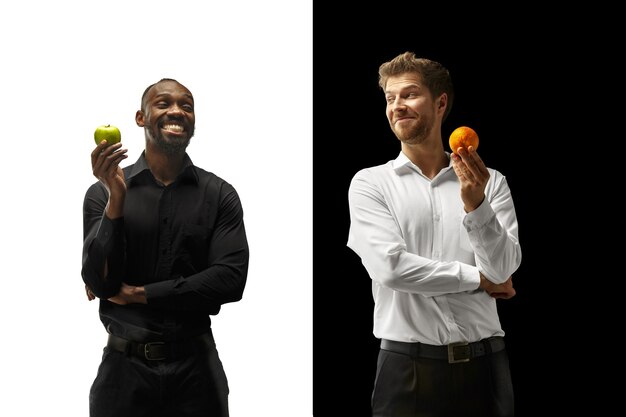 黒と白の背景に新鮮な果物を食べる男性。幸せな笑顔のアフロと白人男性。健康的な食事と食事の概念