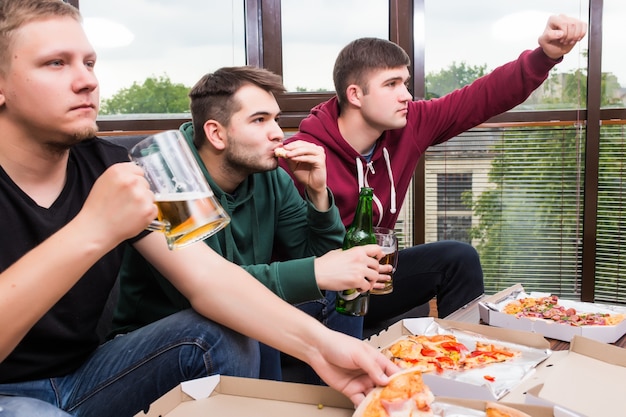 Men fans watching football on TV and drink beer. Three men drinking beer and having fun together in the bar