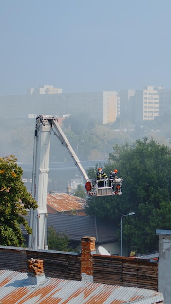 Men from fire department using firetruck to help firefighters on building. Firemen saving house on fire with equipment and water to extinguish flames and fumes in city neighbourhood