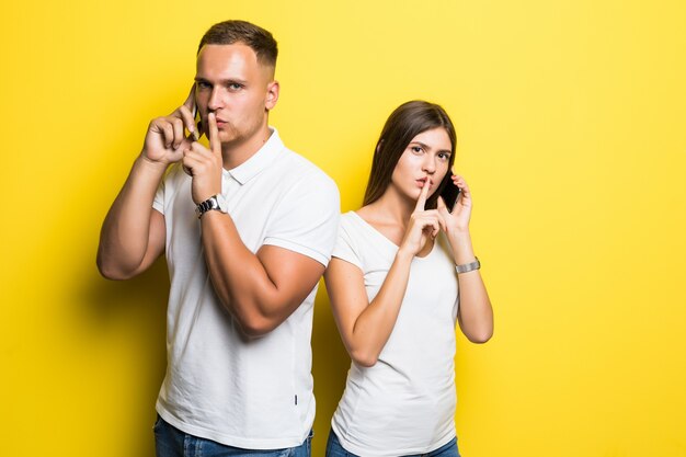 Men and girl please be quiet while talking on their mobile phones isolated on yellow