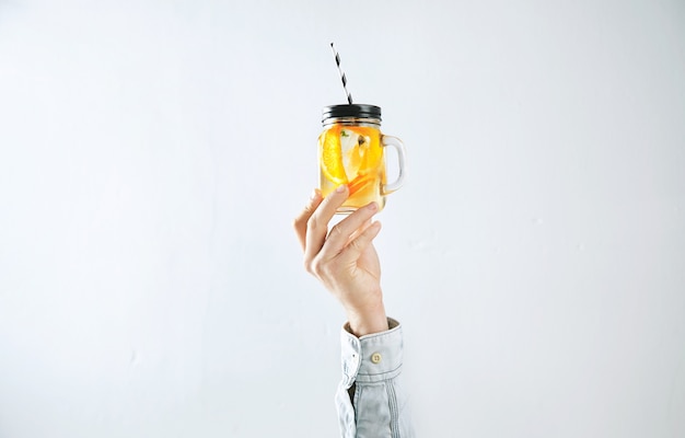 Men hand presents homemade cold lemonade from oranges, sparkling water and ice cubes isolated on white.