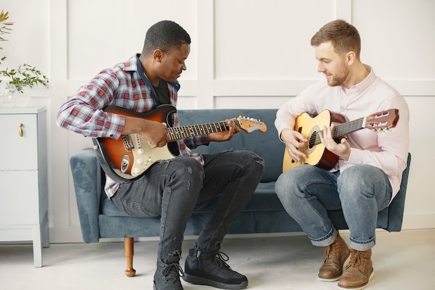 男性はギターを弾きます。音楽を書く。アフリカ人と白人男性。