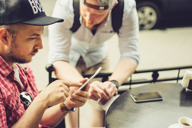 men share news, photos, video on the smartphone. A man shows a friend an application in a mobile phone. Friends with a smartphone, technology.