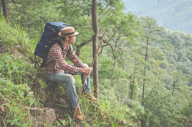 男性は座って、熱帯林の山々をバックパックで眺めます。冒険、旅行、登山。