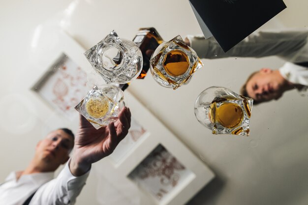 Men take glasses with whisky from a glass table 