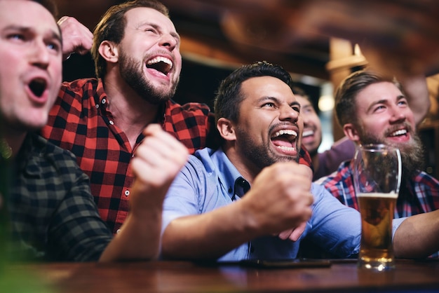 Free photo men watching television and cheering for team