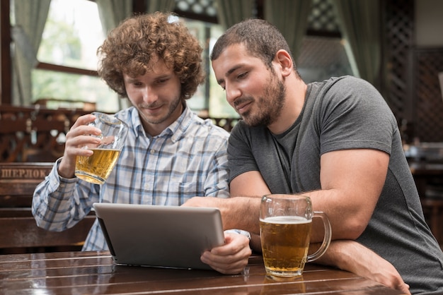 バーでタブレットを使用しているビールを持つ男性