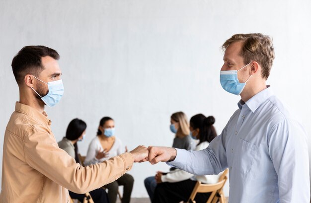 Мужчины в медицинских масках бьют друг друга кулаками на сеансе групповой терапии