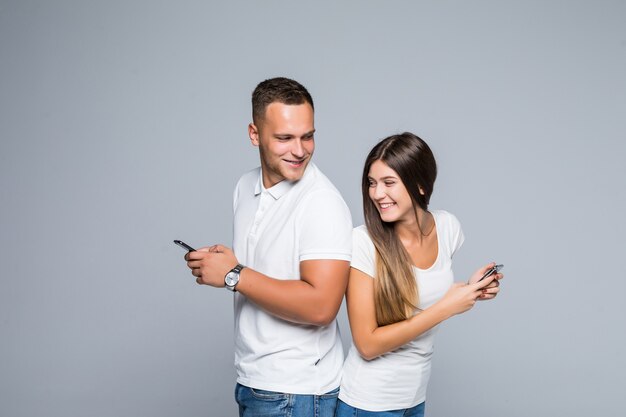 Men and woman smiling couple standing with mobile phones in their hands isolated on grey background