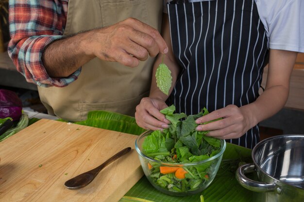 Men and women are helping to separate the vegetables in a clear cup in the kitchen with a red brick wall.