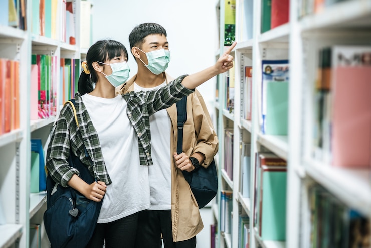 無料Photo リュックを背負って図書館で本を探す男女。