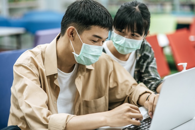 Men and women wear masks and use a laptop to search for books in the library.