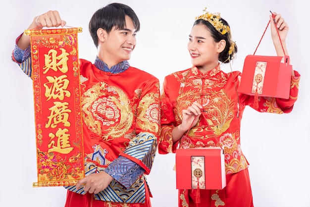 Free photo men and women wearing cheongsam standing, holding greeting signs and carrying red bags